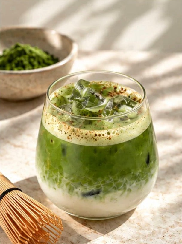 Iced matcha latte with a bamboo whisk and a bowl of matcha powder